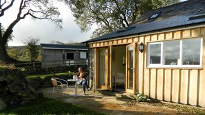 Un edificio rustico in legno con fondamenta in pietra, un patio con tavolo e sedie, e un muro in pietra sullo sfondo.