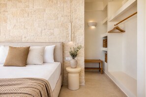 A bedroom with a stone-textured wall, a bed with white bedding, a bedside table with a vase, and a wooden bench.