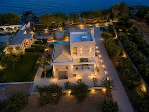 A modern villa with a swimming pool, stone exterior, and a view of the sea.