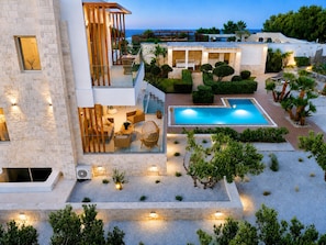 A modern villa with a swimming pool, outdoor seating, and a view of the sea.