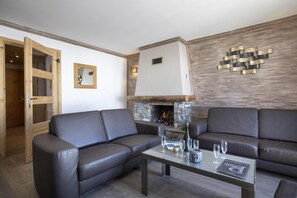 Uma sala de estar moderna com dois sofás de couro escuro, uma mesa de centro de vidro e uma lareira de pedra.