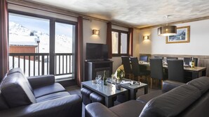 A hotel room with a balcony, a dining area, and a seating area with leather sofas and chairs.
