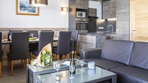 A modern living room with a glass coffee table, black leather sofa, and dining area with wooden chairs.