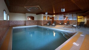 An indoor swimming pool with a tiled floor, wooden ceiling, and a mural on the wall.