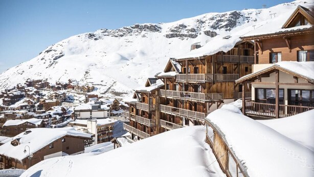 A snow-covered mountain town with wooden buildings, balconies, and a clear sky.