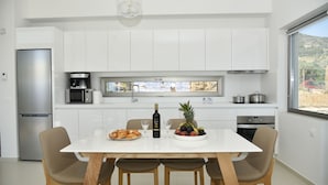 Une cuisine moderne avec des meubles blancs, un réfrigérateur en acier inoxydable, une machine à café et une table à manger avec des chaises.