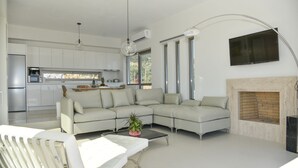 Ein modernes Wohnzimmer mit einem Ecksofa, einem Couchtisch mit Pflanze, einem Kamin und einer Küche im Hintergrund.