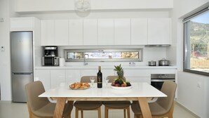 Eine moderne Küche mit weißen Schränken, einem Edelstahlkühlschrank, einer Kaffeemaschine und einem Esstisch mit Stühlen.
