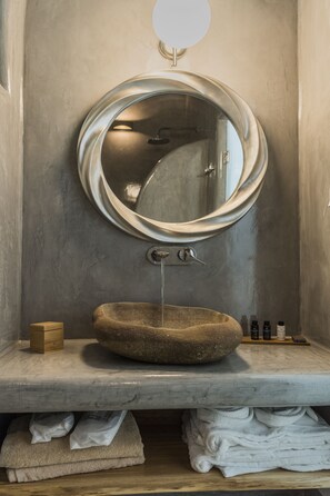 Un baño con un espejo redondo, un lavabo de piedra y toallas dobladas con cuidado.