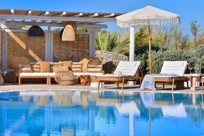 Een zwembadgedeelte met ligbedden, een pergola en een geweven parasol.