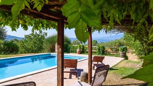 Zona de piscina con sillas de madera y una pérgola.