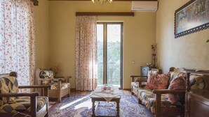 A cozy living room with a sofa, chairs, a table, and a large window with curtains. - Cosi Apartment in village (Lakka Paxos)