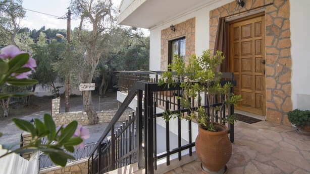 A stone building with a wooden door, a black metal railing, and a potted plant on the porch. - Cosi Apartment in village (Lakka Paxos)