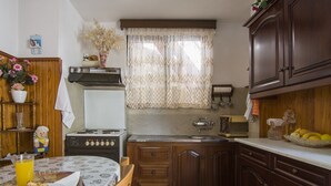 A compact kitchen with wooden cabinets, a stove, and a dining area with a table and chairs. - Cosi Apartment in village (Lakka Paxos)