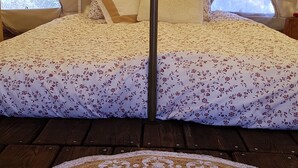 A tent with a bed featuring floral bedding, a circular woven rug, and a view of trees through the tent's openings.