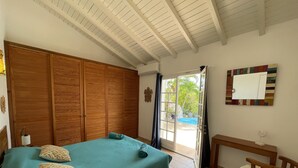 Een slaapkamer met een bed, een houten kledingkast, een bureau en uitzicht op een zwembad.