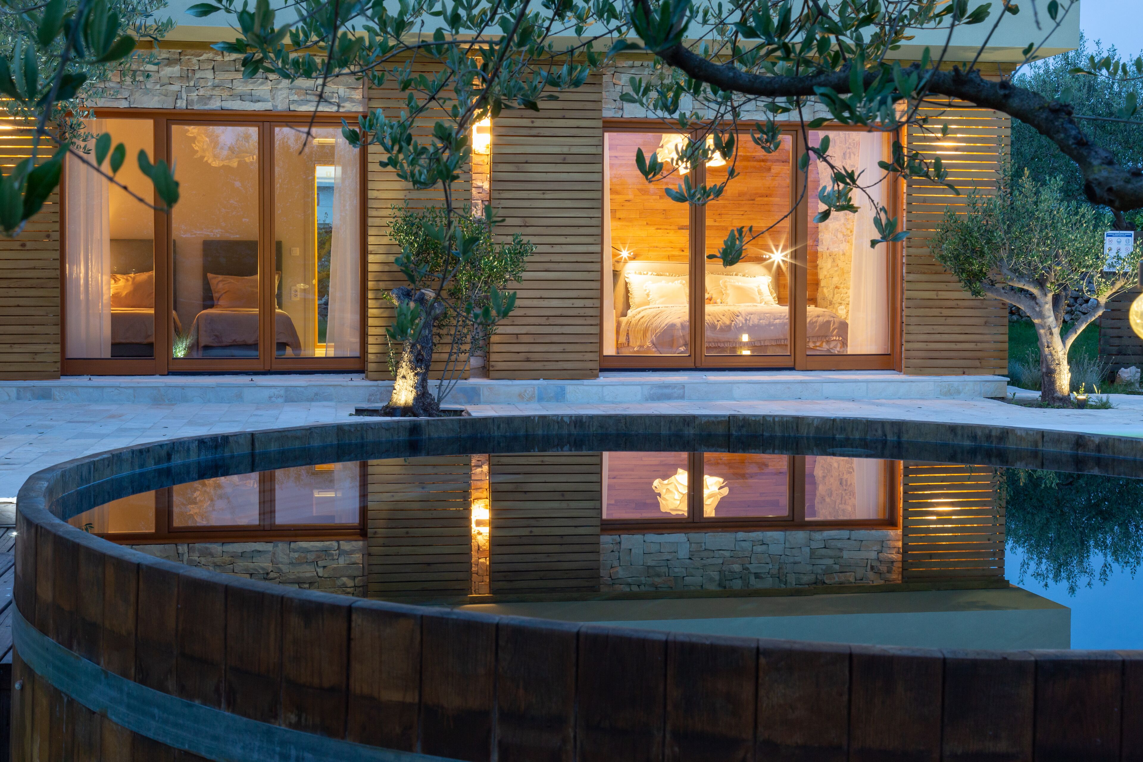 A modern house with large glass doors leading to a bedroom, a stone wall, and a wooden deck.