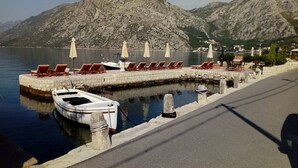 A waterfront area with a row of sun loungers and umbrellas, a small boat docked, and a mountain in the background. - Exotic,sunny and peacfull (Dobrota)