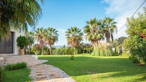 A well-maintained garden with palm trees, a stone pathway, and a house with a dark door. - Orange Tree Garden Villa (Chania)
