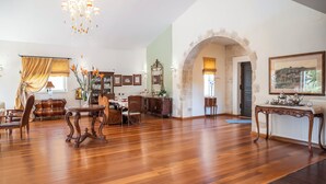 A spacious living room with a wooden floor, a dining table with chairs, a chandelier, and a large painting on the wall. - Orange Tree Garden Villa (Chania)