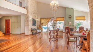 A spacious living area with a wooden floor, a chandelier, a dining table with chairs, and a fireplace. - Orange Tree Garden Villa (Chania)