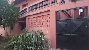 Een roze gebouw met een decoratieve gevel, een zwart hek en een kleine tuin met planten.