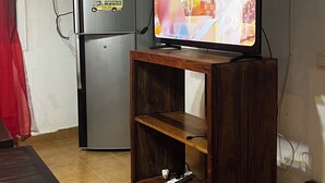 Een woonkamer met een televisie op een houten standaard, een koelkast en een eettafel.