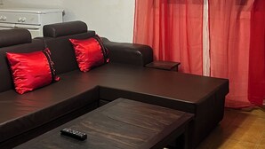 Een woonkamer met een hoekbank, een salontafel en een rood gordijn.