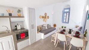 Een compacte keuken met een ingebouwde oven, een eethoek met een tafel en stoelen, en een klein zithoekje met kussens.