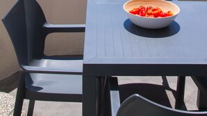 Een tafel met een schaal tomaten op een balkon met uitzicht op een blauwe zee en een zeilboot.