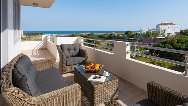 Un balcone con mobili in vimini, una ciotola di frutta e vista sul mare e sugli edifici.