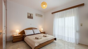Una camera da letto con un letto grande, una testiera in legno, due comodini con lampade, un lampadario e una finestra con tende leggere.