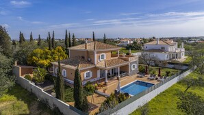Une maison à deux étages avec une piscine, entourée d’arbres et sous un ciel dégagé.