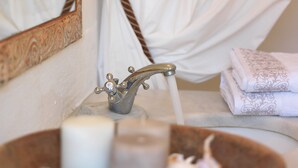 Une salle de bain avec un lavabo en bois contenant des bougies, un miroir doté d’un cadre orné et une serviette à motifs floraux.