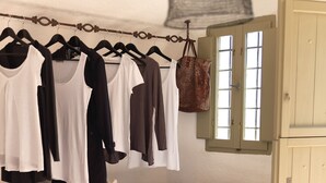 Une pièce comprenant un fauteuil blanc, une étagère en bois avec des chaussures et un portant à vêtements sur lequel sont suspendus différents articles.