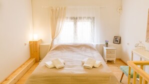 A bedroom with a bed, bedside table, nightstand, and a window with curtains.