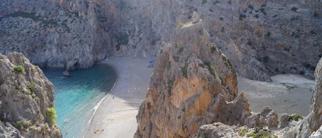 A rocky coastal landscape with a narrow beach and clear blue waters.
