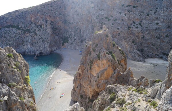 A rocky coastal landscape with a narrow beach and clear blue waters.