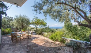 Une terrasse extérieure avec une table et des chaises, un mur en pierre et une vue sur la mer.