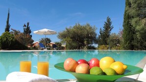 Een zwembadlandschap met een fruitschaal, een glas sinaasappelsap en een witte handdoek.