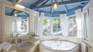 Une salle de bain avec une baignoire sur pieds, un lavabo, un grand miroir et une fenêtre avec des rideaux.