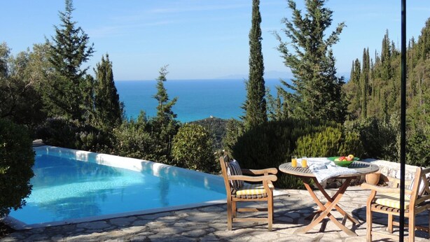 Une piscine offrant une vue dégagée sur la mer, entourée d’arbres et agrémentée d’une table en bois avec des chaises.