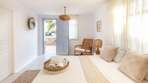 Ein Schlafzimmer mit einem Bett, einem Sessel, einem Wäschekorb mit Handtüchern, einer Pendelleuchte und einer Tür, die nach draußen führt.