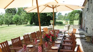 An outdoor dining area with wooden tables and chairs, a large umbrella, and a stone wall in the background. - Enchanting Château with en-suites, Pool, Tennis, Grand Piano, BBQ, Fast WiFi (Thézac)