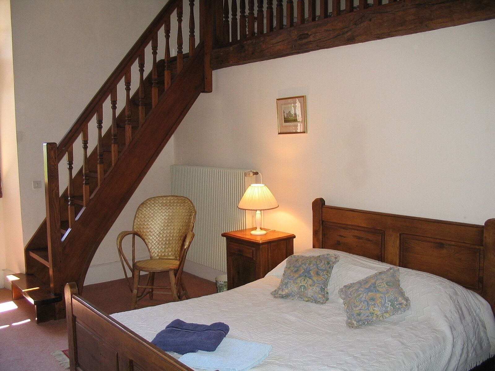 Une chambre à coucher avec un lit en bois, une chaise, une table de chevet avec une lampe et un escalier.