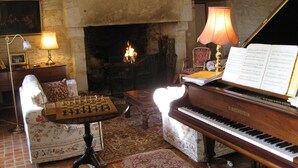 A room with a grand piano, a chessboard, a fireplace, and a piano bench. - Enchanting Château with en-suites, Pool, Tennis, Grand Piano, BBQ, Fast WiFi (Thézac)