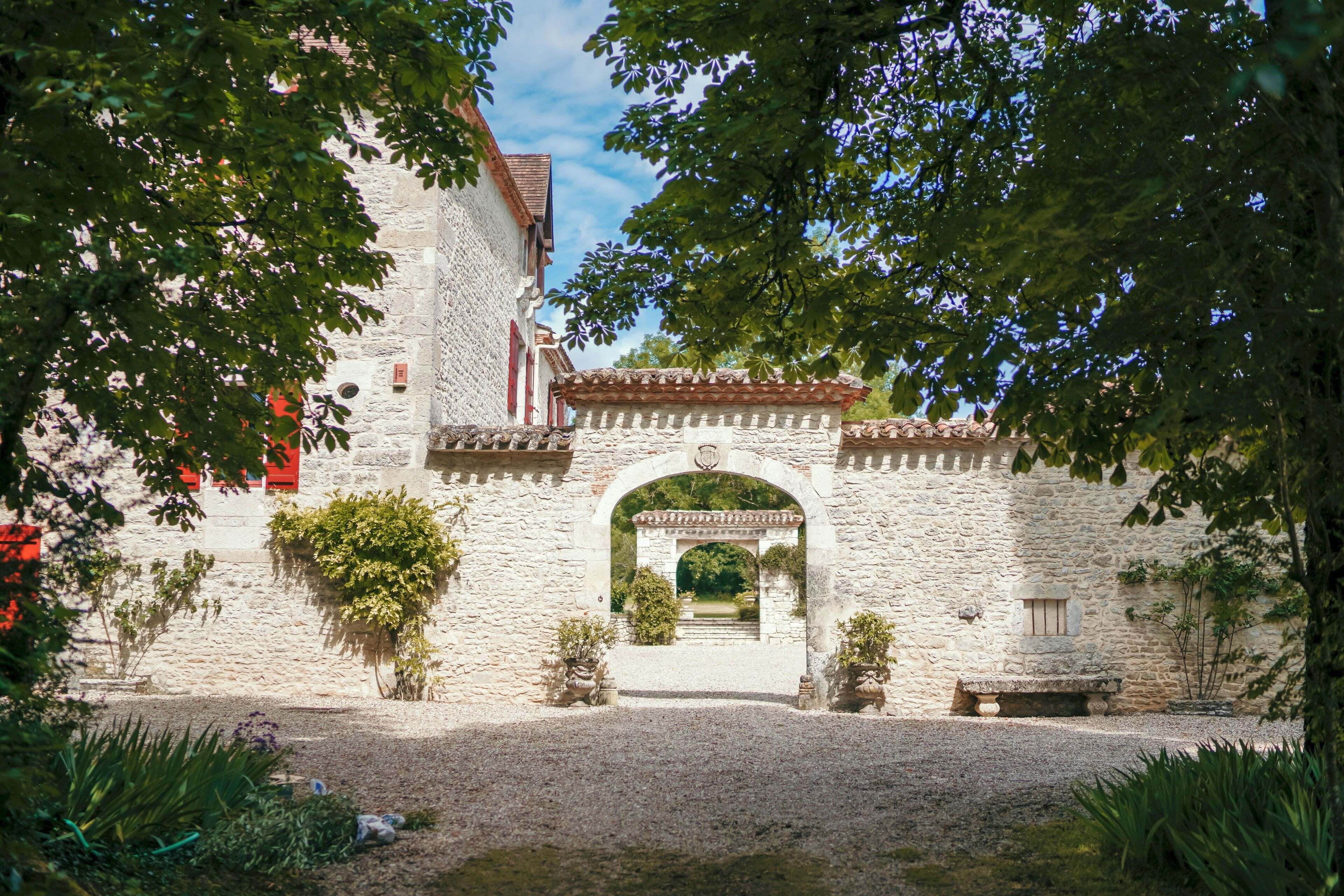 A stone building with a central archway, surrounded by greenery and potted plants.