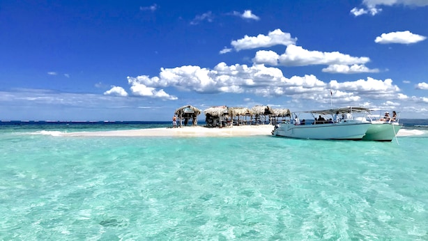 A beach with clear turquoise water, a boat, and thatched-roof huts in the background. - A Few Steps From The Gorgeous Beach Of Punta Rucia! (Punta Rucia)