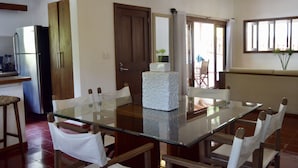 A dining area with a glass-top table, white upholstered chairs, and a wooden door. - A Few Steps From The Gorgeous Beach Of Punta Rucia! (Punta Rucia)