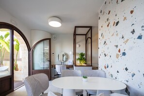 A modern dining area with a round table, grey chairs, a potted plant, and a terrazzo wall. - Villa Nayana - Shoreline Calm by etouri (Rethymno)